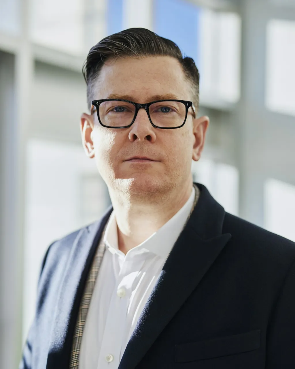 Professional headshot of a man in glasses and a navy blazer